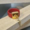 Bague en cuir rouge cousu et bélière carrée dorée avec pampille oiseau